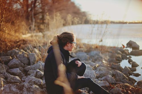 young woman sitting alone on rocky shore during cold weather - holidays