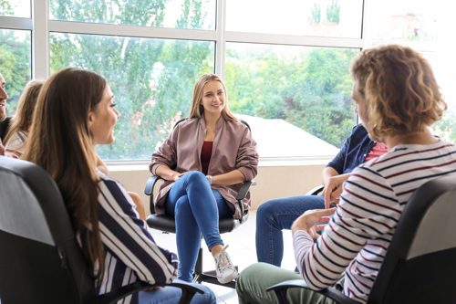 young adults sitting in chairs in a circle - group therapy