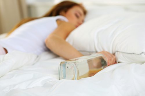 young woman passed out in bed holding liquor bottle - blackouts