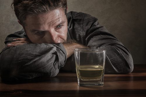 concerned man looking at glass of liquor on table - alcohol use disorder