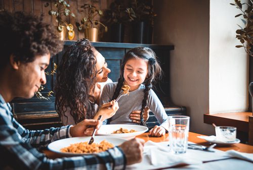 young Hispanic family at table enjoying meal together - parenting