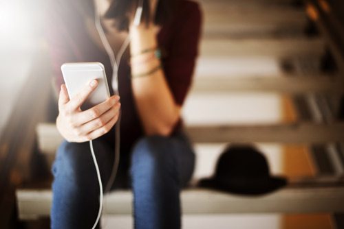 young woman sitting on stairs listening to headphones - motivational podcasts