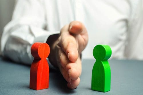 man's hand placed between a red wooden figure and a green wooden figure - controversy - addiction