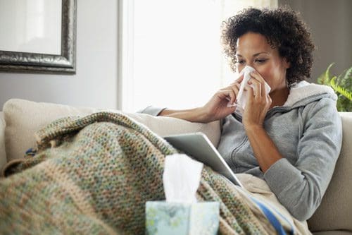 sick woman at home on couch blowing her nose into a tissue - immune system