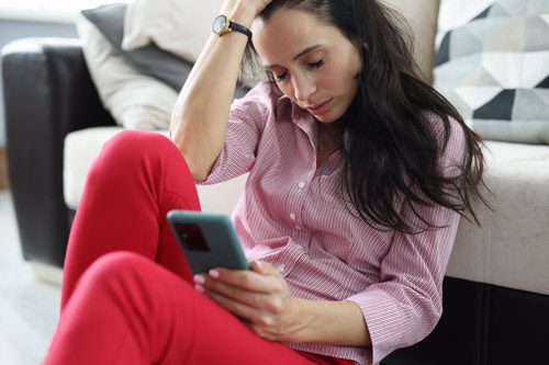 woman in her thirties sitting on the floor at home holding her head with one hand and a cell phone with the other - antidepressant withdrawal