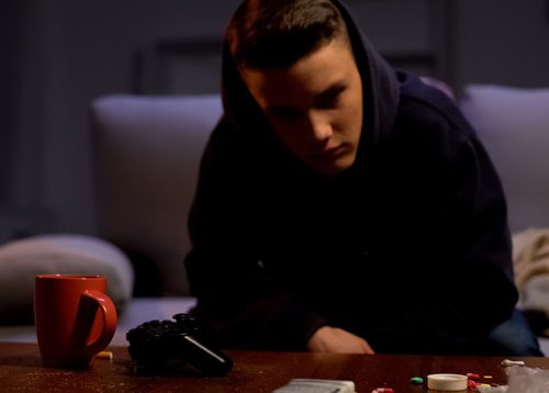 young man sitting on couch in front of table with various drugs - cocaine addiction