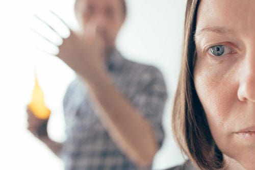 cropped closeup of a woman's face with a blurred man holding a beer in the background - alcohol addiction