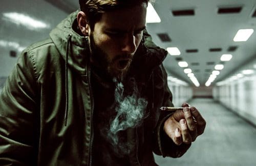 young man smoking a marijuana cigarette in a subway tunnel