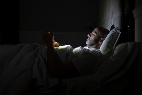 man using his cell phone in bed in a completely dark room - substitute addictions