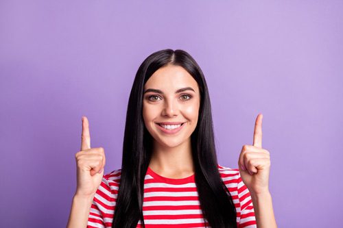 smiling brunette pointing up with both hands against a pretty medium purple background - returning to work