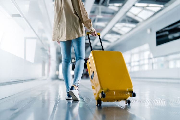 Woman walking through airport with yellow suitcase - traveling