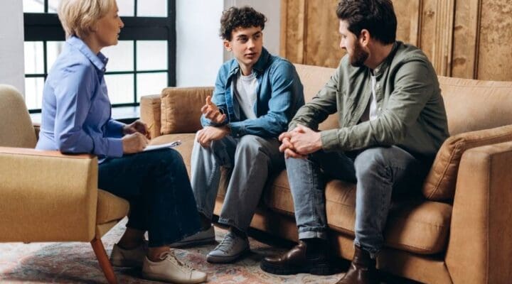 Father and teenage son visiting psychologist, talking together in the office. Family problems, teenage troubles, therapist, advice, help concept