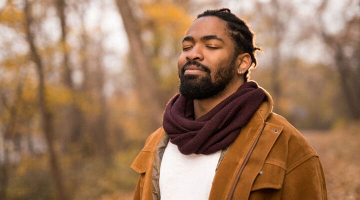 man outside in nature in the fall with his eyes closed, looking content and peaceful