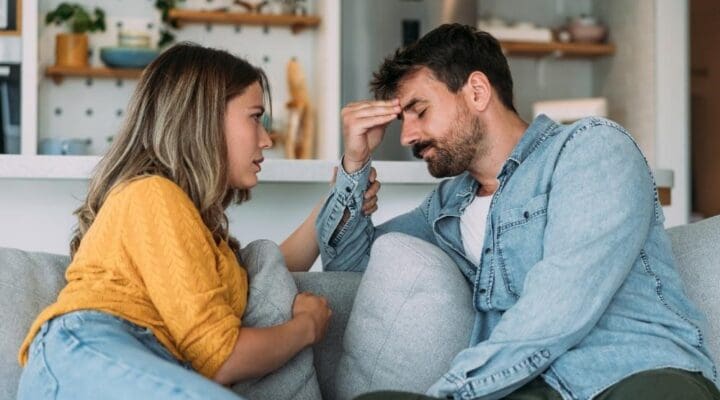 Twin Lakes - How Healthy Boundaries Protect Your Sobriety. A young couple sits on a couch. A woman on the left consoles a frustrated and upset man on the right. The room is well lit and clean