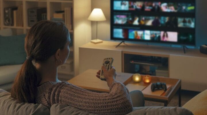 Twin Lakes - Learning to Enjoy Downtime Without Substances. A woman sits on a couch in the evening browsing listings on the TV